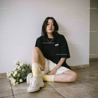 Fashionable Young Woman Sitting on Floor with Flowers and Casual Outfit