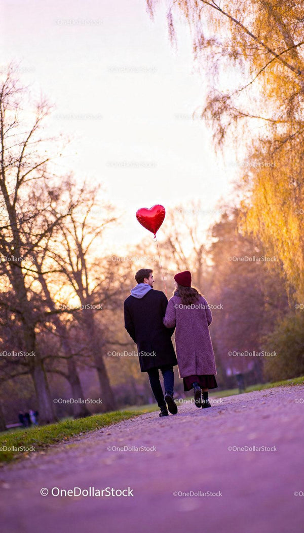 Couple walking together with heart-shaped balloon in park