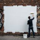 Person painting white rectangle on brick wall outdoors