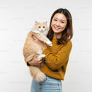 Smiling woman holding fluffy cream cat indoors