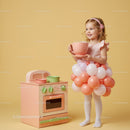 Smiling toddler girl playing with toy kitchen and balloon dress