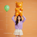 Smiling woman holding large gummy bear toy above head