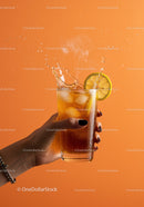 Refreshing iced tea with lemon splash on orange background
