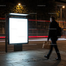Man walking past illuminated blank city billboard at night