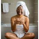 Young Woman with Facial Mask Sitting Cross-Legged in Bathroom