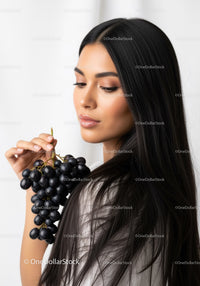 Elegant Woman with Black Hair Holding Grapes in Studio Portrait