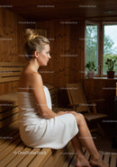 Relaxing Woman Sitting in Wooden Sauna Room with Towels and Potted Plants