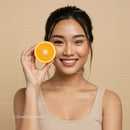 Smiling Woman Holding Orange Half with Bright Skin and Cheerful Expression
