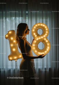 Young woman celebrating eighteenth birthday with glowing balloons