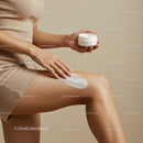 Woman Applying Body Lotion with Skincare Jar on Leg in Neutral Tones