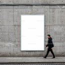 Blurred man walking past blank urban billboard on concrete wall