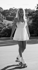 Young woman in white dress roller skating outdoors