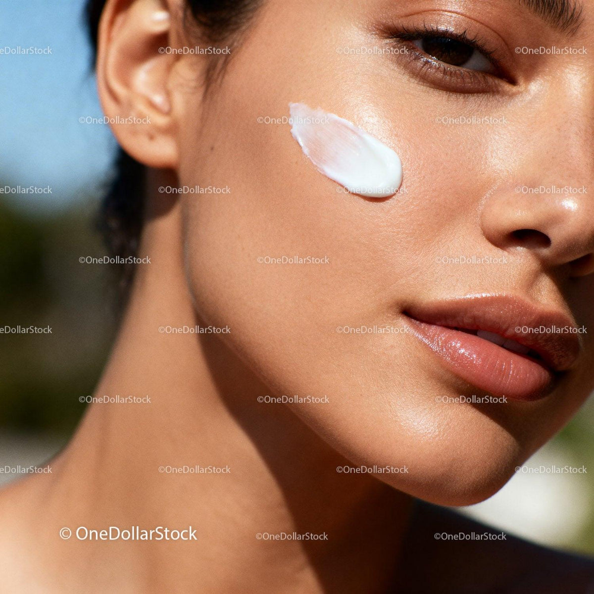 Closeup of woman applying moisturizing cream on cheek