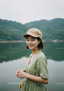 Young Woman Smiling at Lake in Green Dress and Beige Cap