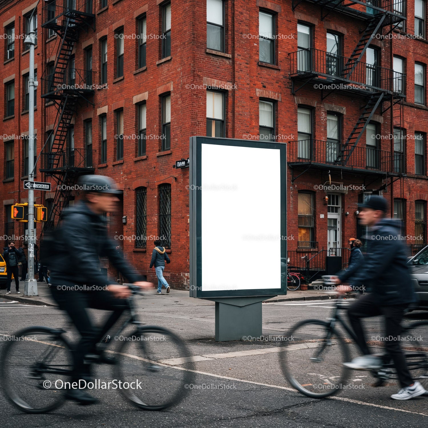 Rowerzyści miejscy mijają pusty billboard w pobliżu ceglanego budynku
