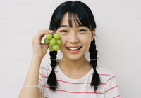 Joyful Girl with Braided Hair Holding Fresh Green Grapes in Bright Indoor Setting