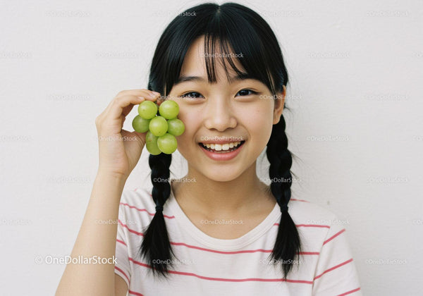 Joyful Girl with Braided Hair Holding Fresh Green Grapes in Bright Indoor Setting