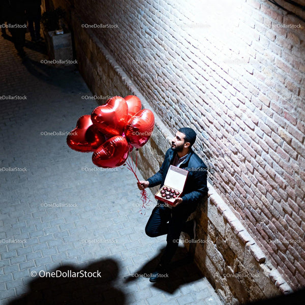 Man holding heart balloons and chocolates in alley
