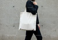 Person carrying blank canvas tote bag on shoulder