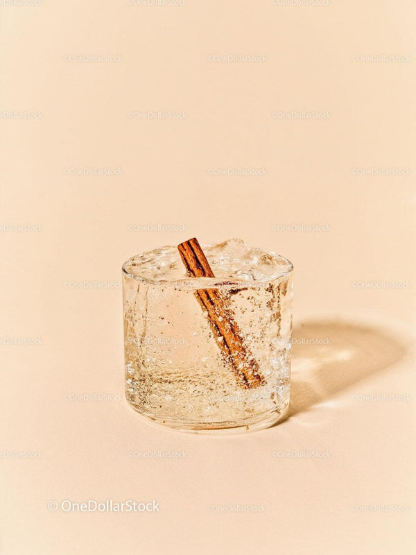 Refreshing iced drink with cinnamon stick on beige background