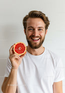 Smiling Young Man with Beard Holding Fresh Grapefruit Slice
