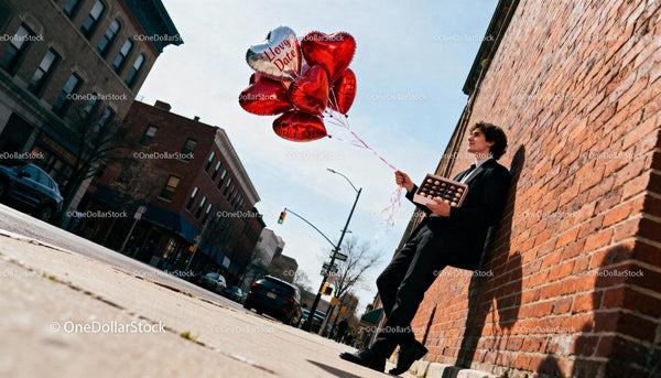 Man in suit holding heart balloons and chocolate box outside