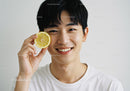 Joyful Young Man Holding Lemon Slice with Bright Smile in Studio