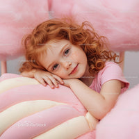Redhead girl resting on large pastel candy cushion
