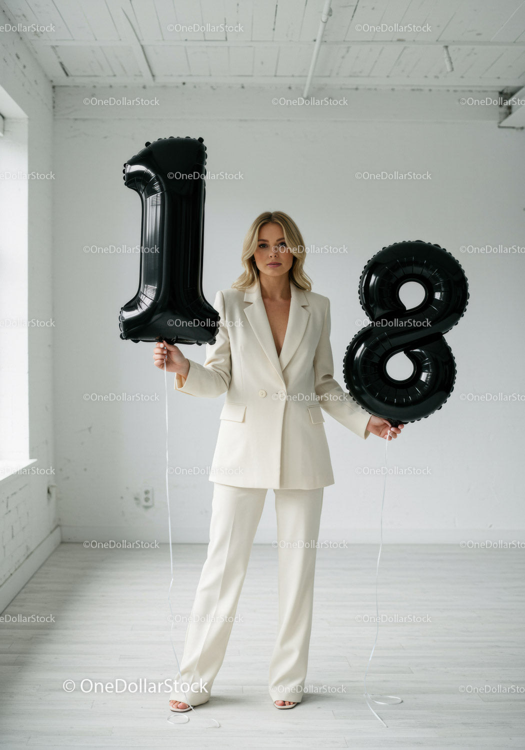 Blondynka w białym kostiumie trzymająca czarne balony z cyframi
