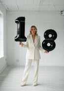 Blonde woman in white suit holding black number balloons