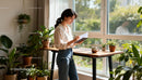 Young woman writing notes by bright window with plants