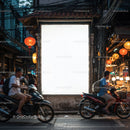 Evening street scene with scooters passing illuminated market stalls