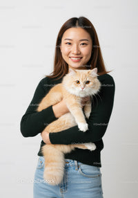 Young woman holding fluffy ginger cat indoors