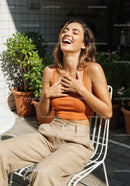 Joyful Woman in Orange Tank Top and Beige Pants Relaxing Outdoors