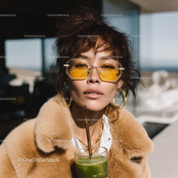 Fashionable woman with yellow sunglasses and fur coat enjoying green juice