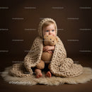 Cute baby wrapped in knitted blanket hugging teddy bear
