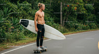 Young Man on Skateboard Holding Surfboard in Nature Setting
