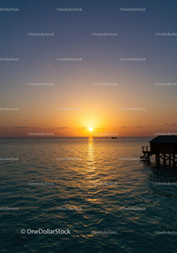 Sunset Over Calm Ocean with Pier and Boat Silhouette