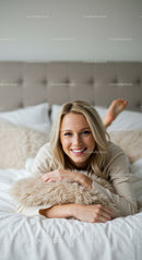 Smiling young woman relaxing on cozy bed with plush pillow