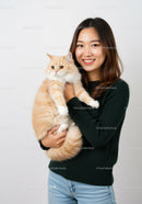 Smiling woman holding fluffy orange cat indoors