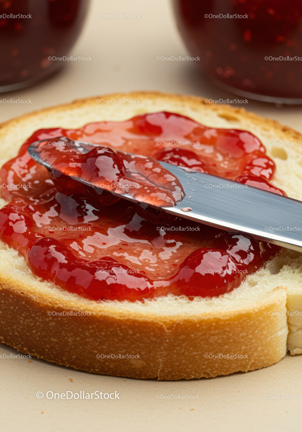 Knife Spreading Red Strawberry Jam on Slice of White Bread