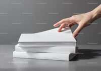 Hand Reaching for a Book from a Stack on Gray Surface