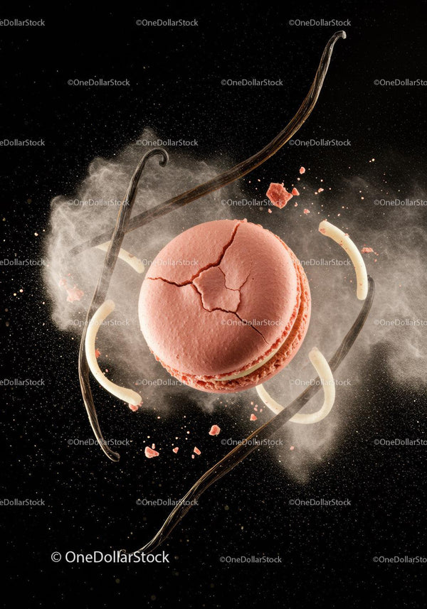 Cracked pink macaron surrounded by vanilla pods and powder