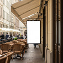 Empty outdoor cafe seating with blank signboard on street