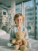 Cheerful Child In Hospital Bed Holding Teddy Bear In Bright Room