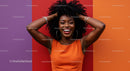 Smiling Woman with Curly Hair in Bright Orange Dress Against Colorful Wall