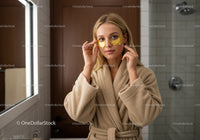 Young woman applying facial under eye masks in bathroom