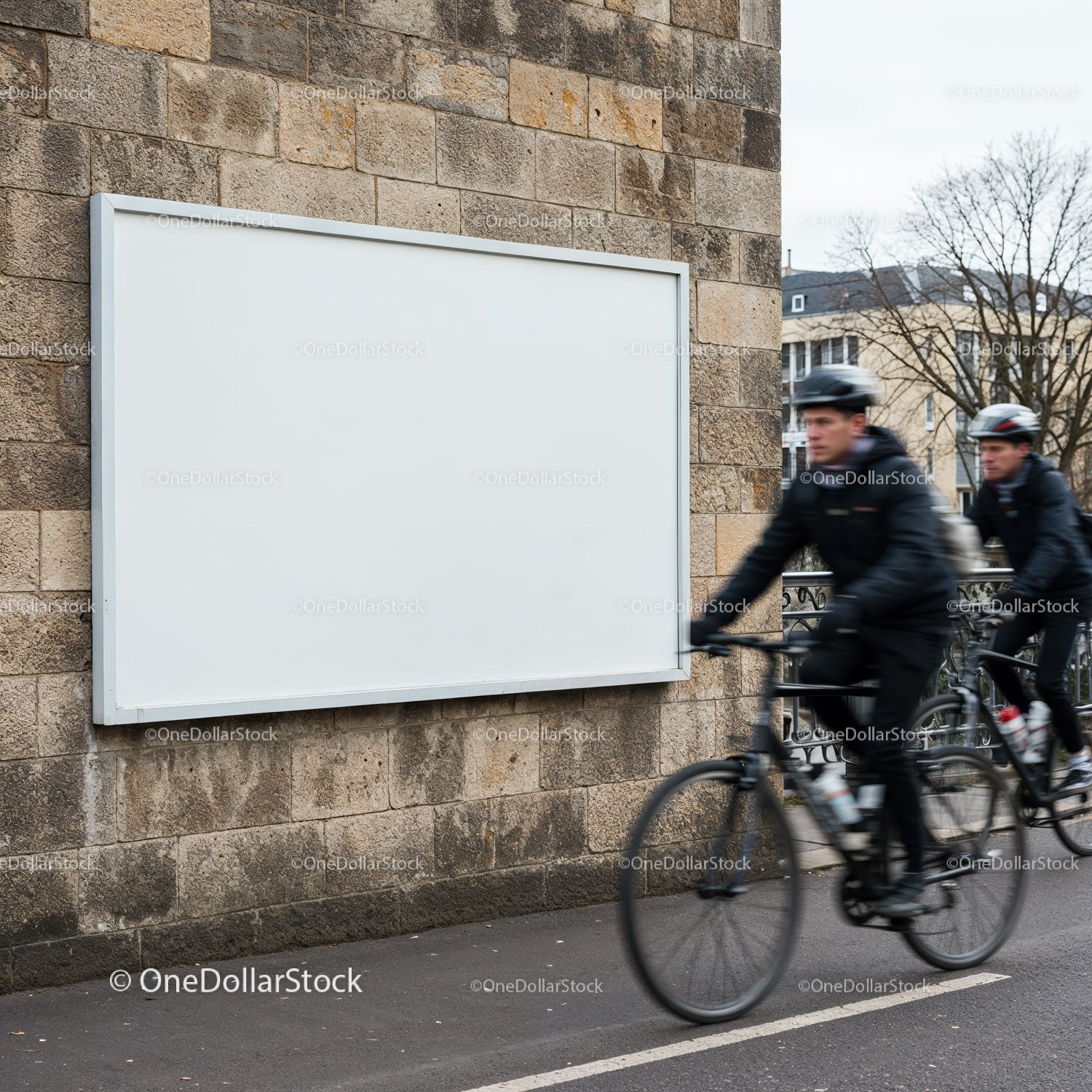 Rowerzyści przejeżdżający obok pustego billboardu na kamiennym murze