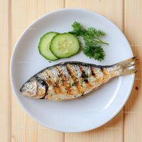 Fresh Grilled Fish with Cucumber Slices and Herbs on White Plate