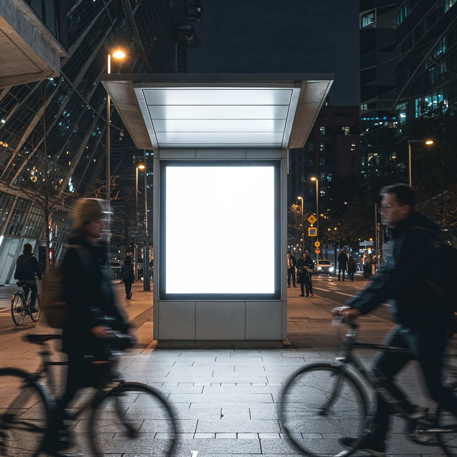 Dojeżdżający do pracy rowerzyści w mieście mijają oświetlony billboard nocą